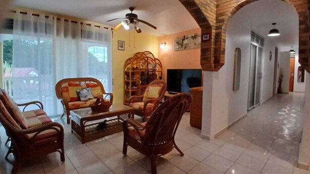 A living room with wicker furniture, a ceiling fan, and a brick archway. - MAGNIFICENT FURNISHED VILLA WITH SWIMMING POOL AND MOUNTAIN VIEW (Petit-Bourg)