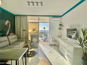 Un salon moderne avec un canapé, une table basse et des fauteuils, un balcon avec vue et un téléviseur fixé au mur.