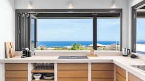 A kitchen with a view of the ocean, wooden cabinets, a coffee maker, and a kettle. - Kas Ubuntu - Villa with Panoramic Ocean Views (Kralendijk)