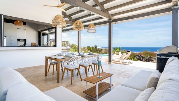 An outdoor dining area with a view of the ocean, a pool, and a covered seating area with a sofa and table. - Kas Ubuntu - Villa with Panoramic Ocean Views (Kralendijk)
