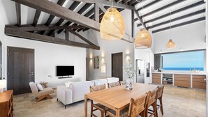 A spacious living area with a wooden dining table, sofas, and a kitchen with a view. - Kas Ubuntu - Villa with Panoramic Ocean Views (Kralendijk)