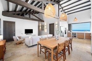 A spacious living area with a wooden dining table, sofas, and a kitchen with a view. - Kas Ubuntu - Villa with Panoramic Ocean Views (Kralendijk)