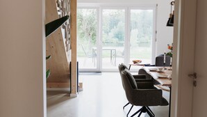 A modern interior with a staircase, a dining area with a table and chairs, and a view through glass doors.