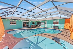 A covered outdoor swimming pool with a glass ceiling, a brick patio, and lounge chairs.