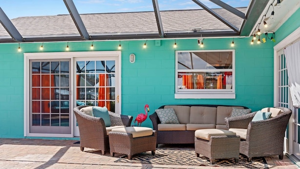 A covered patio with a pool, wicker furniture, and a teal wall.