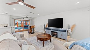 A living room with a sofa, coffee table, TV, fireplace, and a view of a pool.