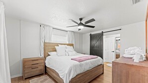 A bedroom with a wooden bed, a nightstand, a bedside table, a ceiling fan, and a view of the outside.