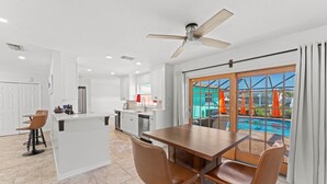 A modern kitchen with a central island, a dining area with two chairs, and a view of a swimming pool through large windows.