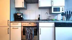 Una cucina compatta con mobili bianchi, forno a incasso, microonde e macchina da caffè.