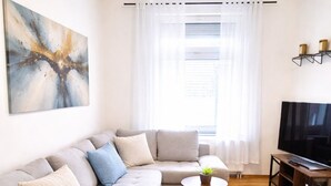Un soggiorno con un divano componibile, due piccoli tavolini rotondi, un televisore a schermo piatto e un grande quadro astratto appeso alla parete.