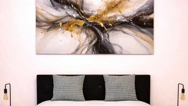 Una camera da letto con un letto, due cuscini, un quadro appeso al muro e due lampade sui comodini.