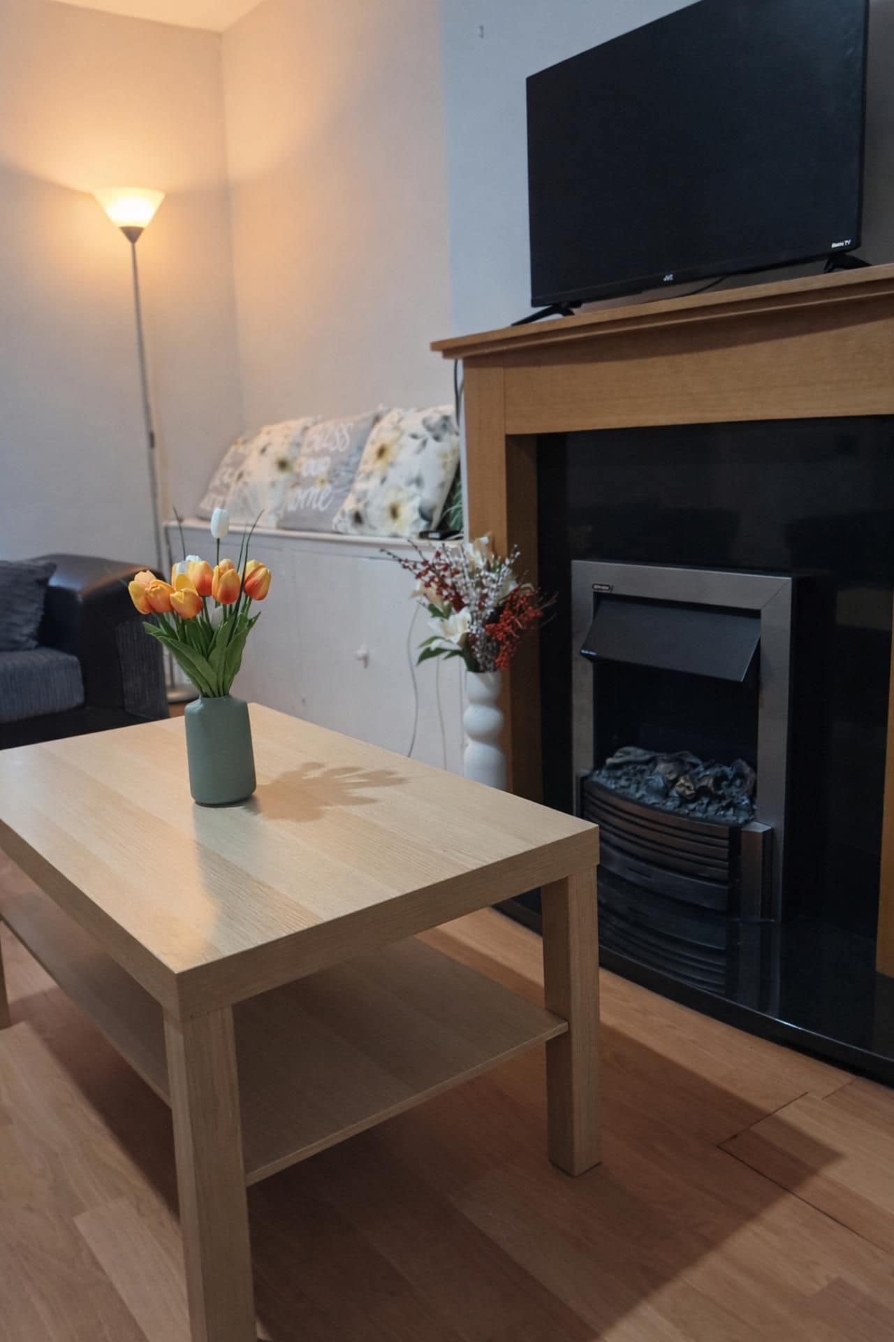 A living room with a wooden table, a vase of flowers, a fireplace, and a television on a stand.