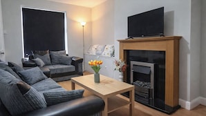 A modern living room with a sofa set, a wooden coffee table, a fireplace, and a flat-screen TV. - 2 Bed Home - Parking, Wifi, Smart Tv (Nottingham)