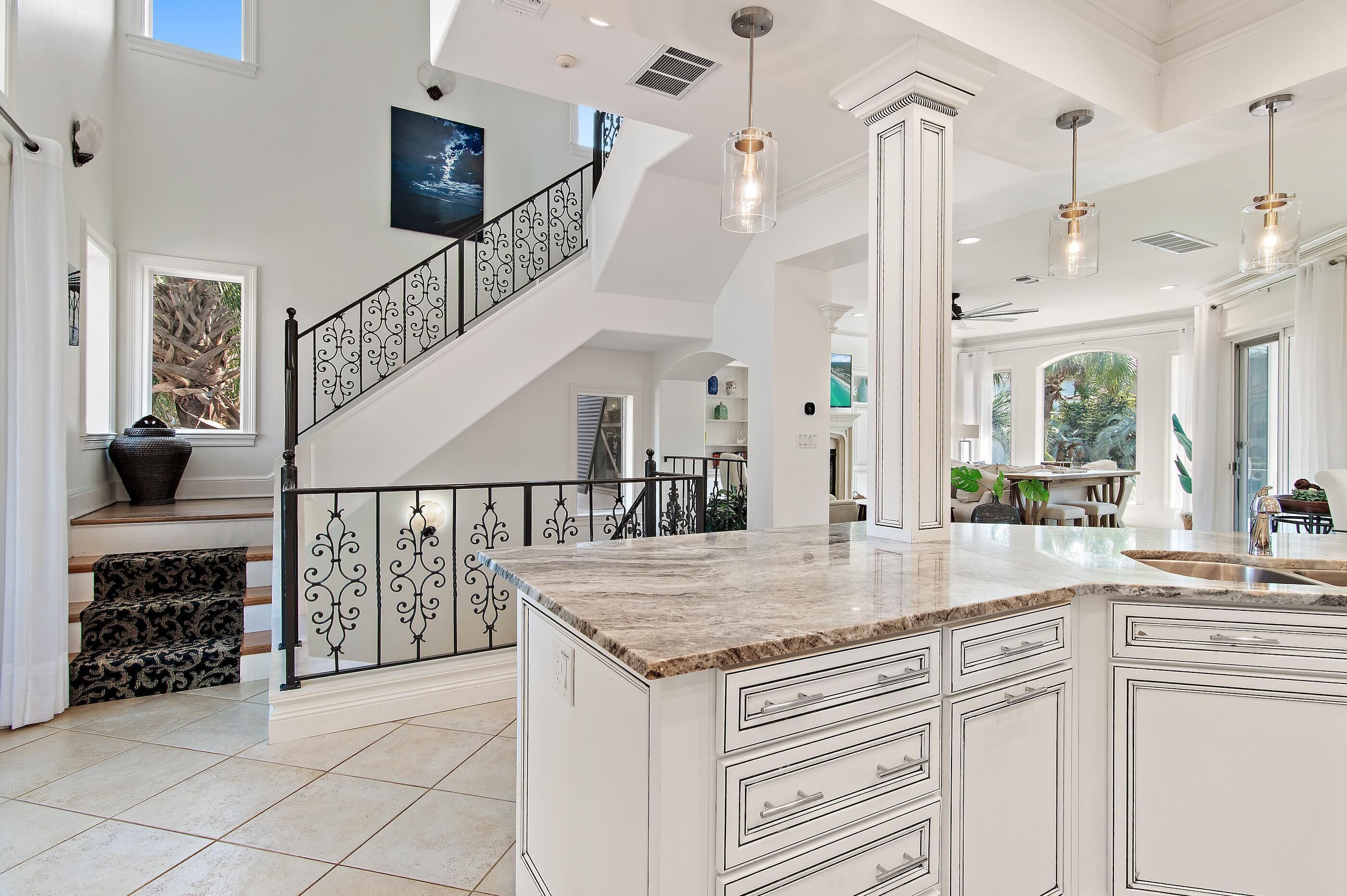 Una cocina amplia con una isla grande, una escalera con barandillas ornamentales y vistas al exterior.