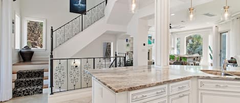 Una cocina amplia con una isla grande, una escalera con barandillas ornamentales y vistas al exterior.