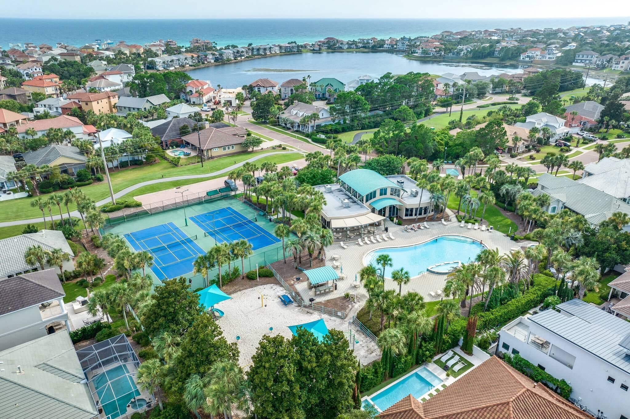 Vista aérea de una zona residencial con una piscina grande, canchas de tenis y un club social.