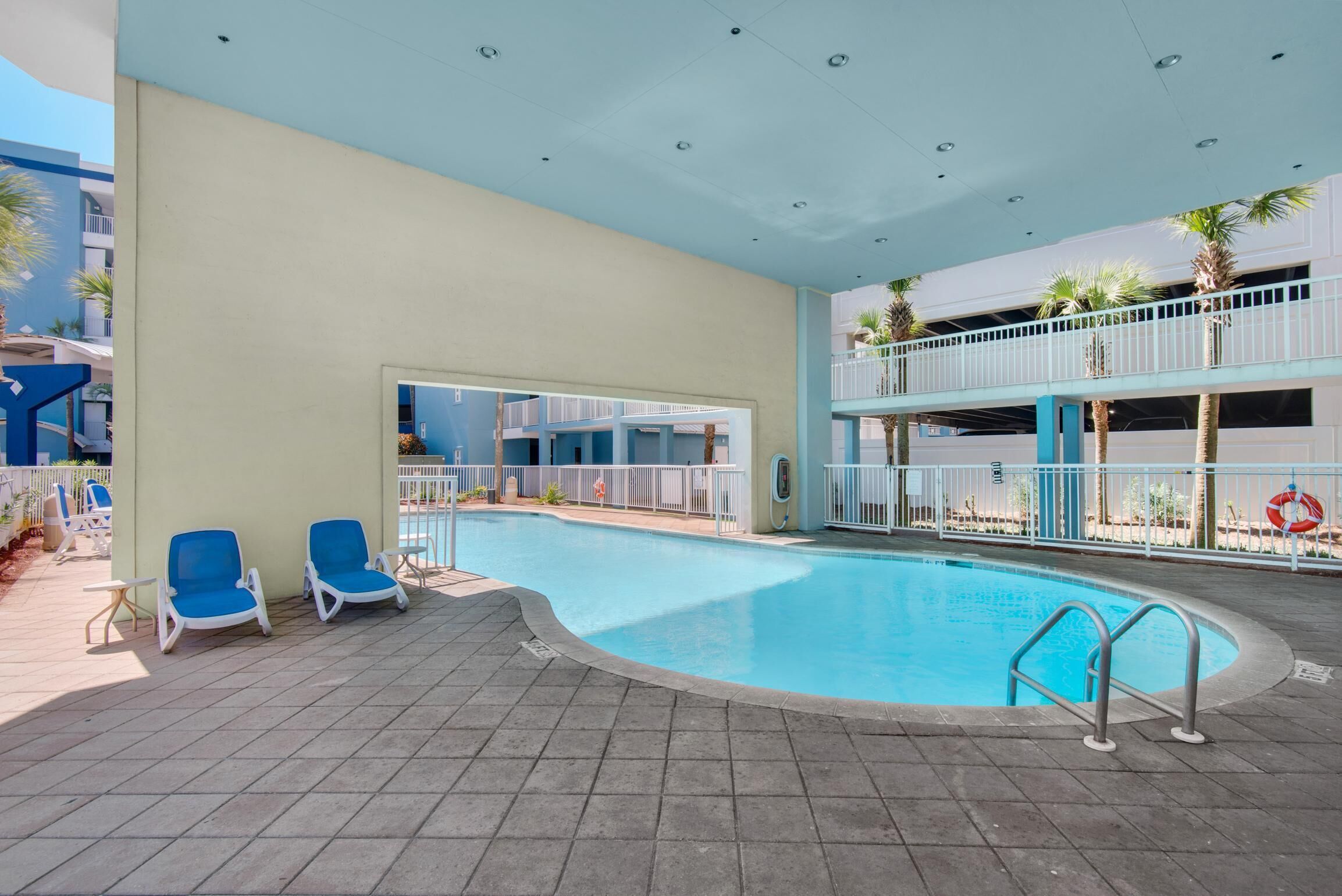 Une piscine avec des chaises bleues, un balcon et une bouée de sauvetage.