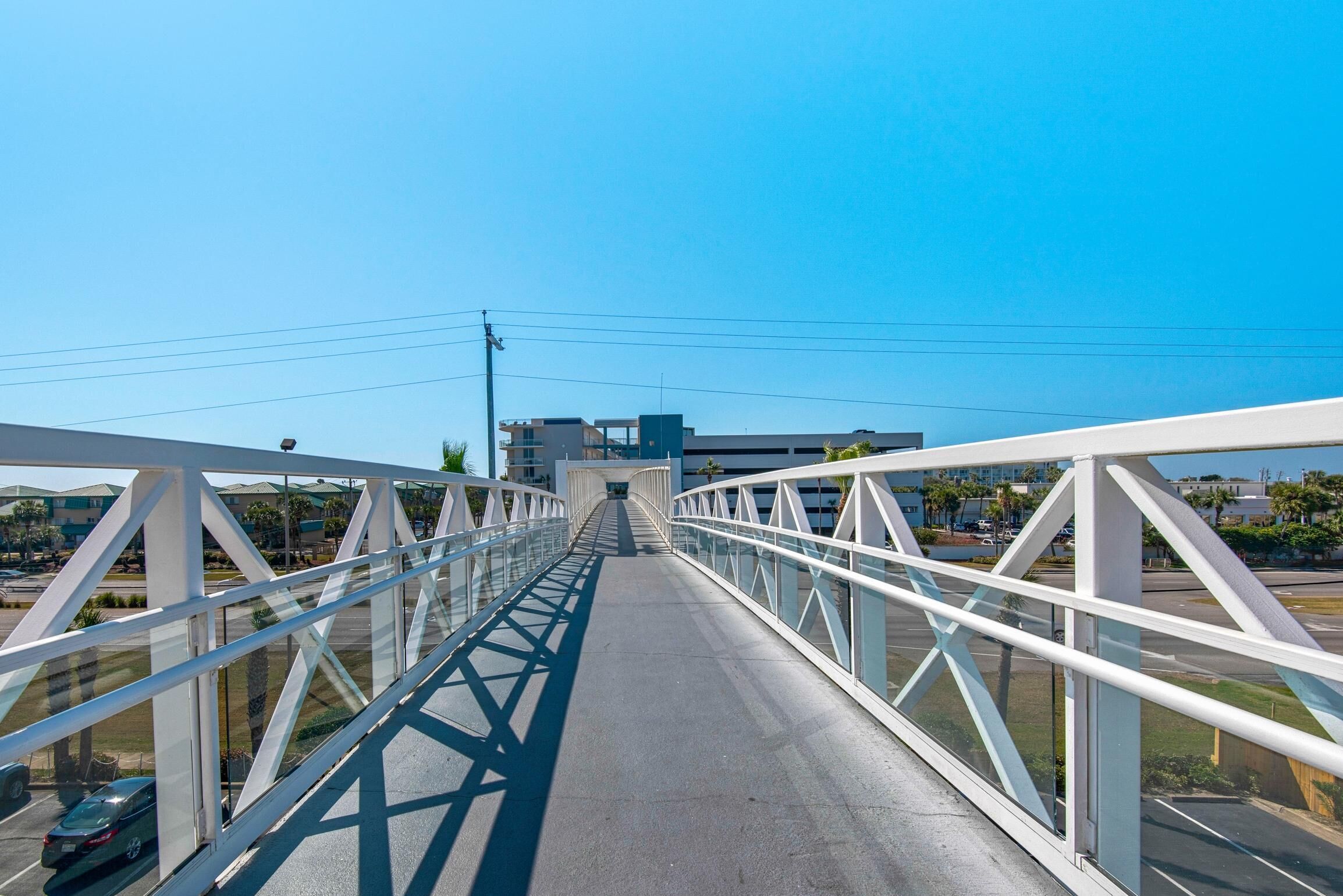 Un puente peatonal con barandillas blancas y paneles de vidrio, que conduce a un edificio de diseño moderno.