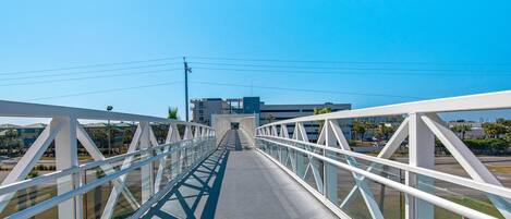 Un puente peatonal con barandillas blancas y paneles de vidrio, que conduce a un edificio de diseño moderno.