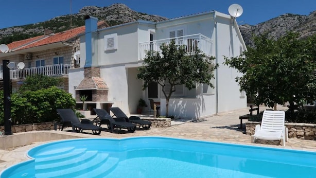 A poolside area with lounge chairs, a barbecue, and a view of a mountainous landscape. - Sunset Bay Villa Kevin (Orebic)