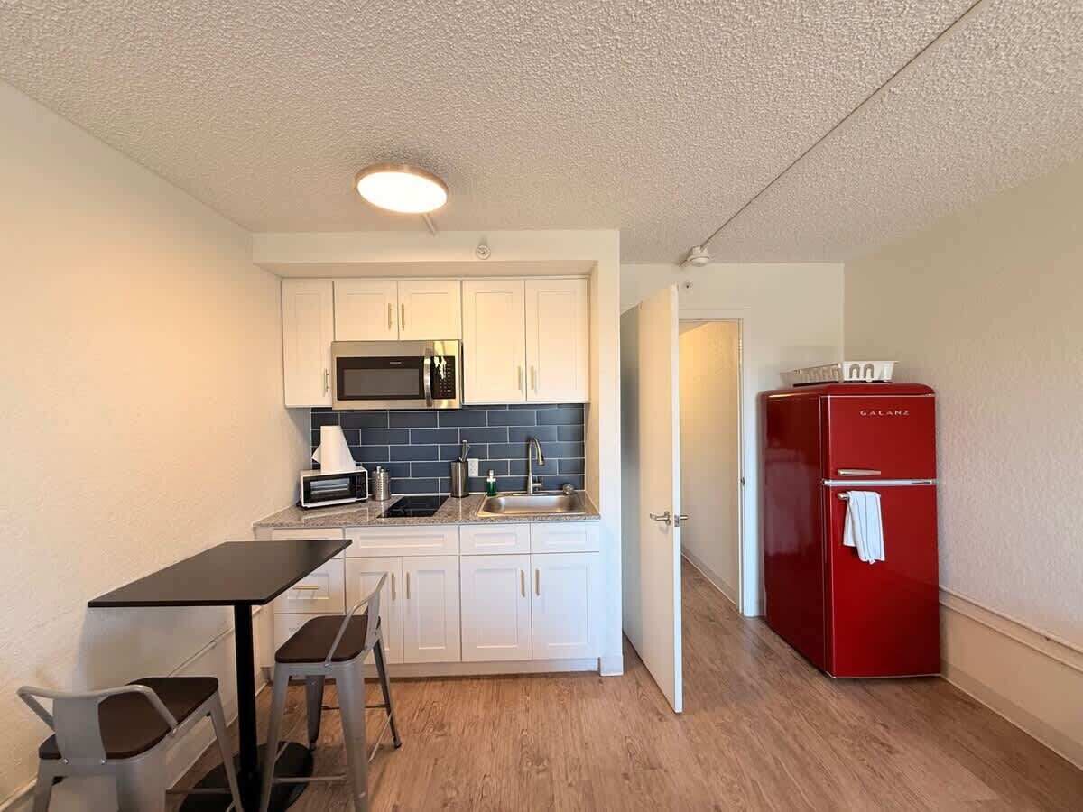 Cocina compacta con armarios blancos, microondas, pileta y refrigerador rojo.