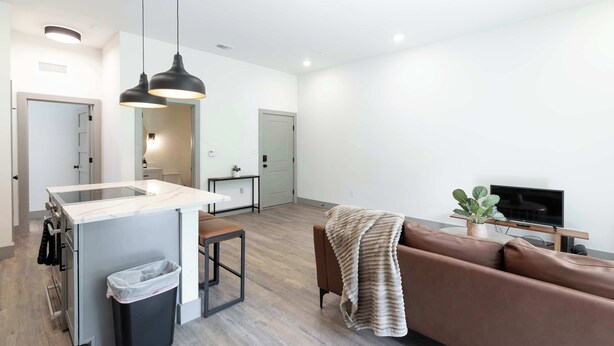 Una cocina moderna con una isla central, una zona de comedor con banco, un sofá y un televisor.