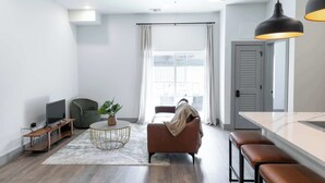 Een moderne woonkamer met een bank, een salontafel, een televisie en een eethoek met krukken.