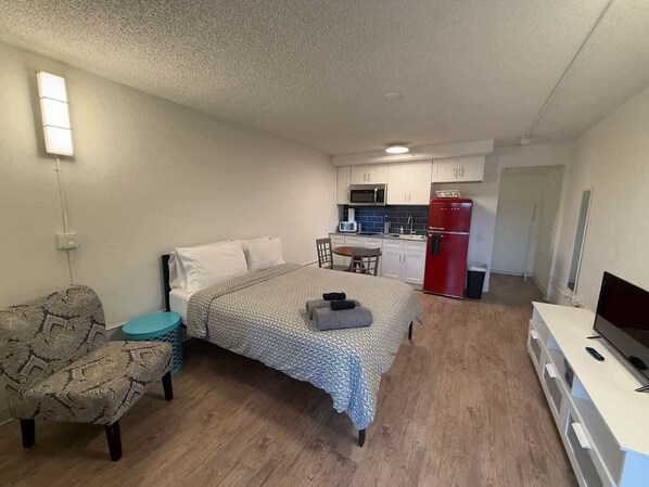A compact room with a bed, a small seating area, a kitchenette, and a TV. - [04] ATX Studio: 1 Queen, Dog Park, Laundry Access (Austin)