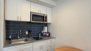 Eine kompakte Küche mit weißen Schränken, einer Mikrowelle, einem Toaster und einem Holztisch.
