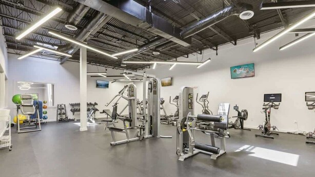 Een sportschool met diverse fitnessapparaten, een tv aan de muur en een plafond met zichtbare balken.