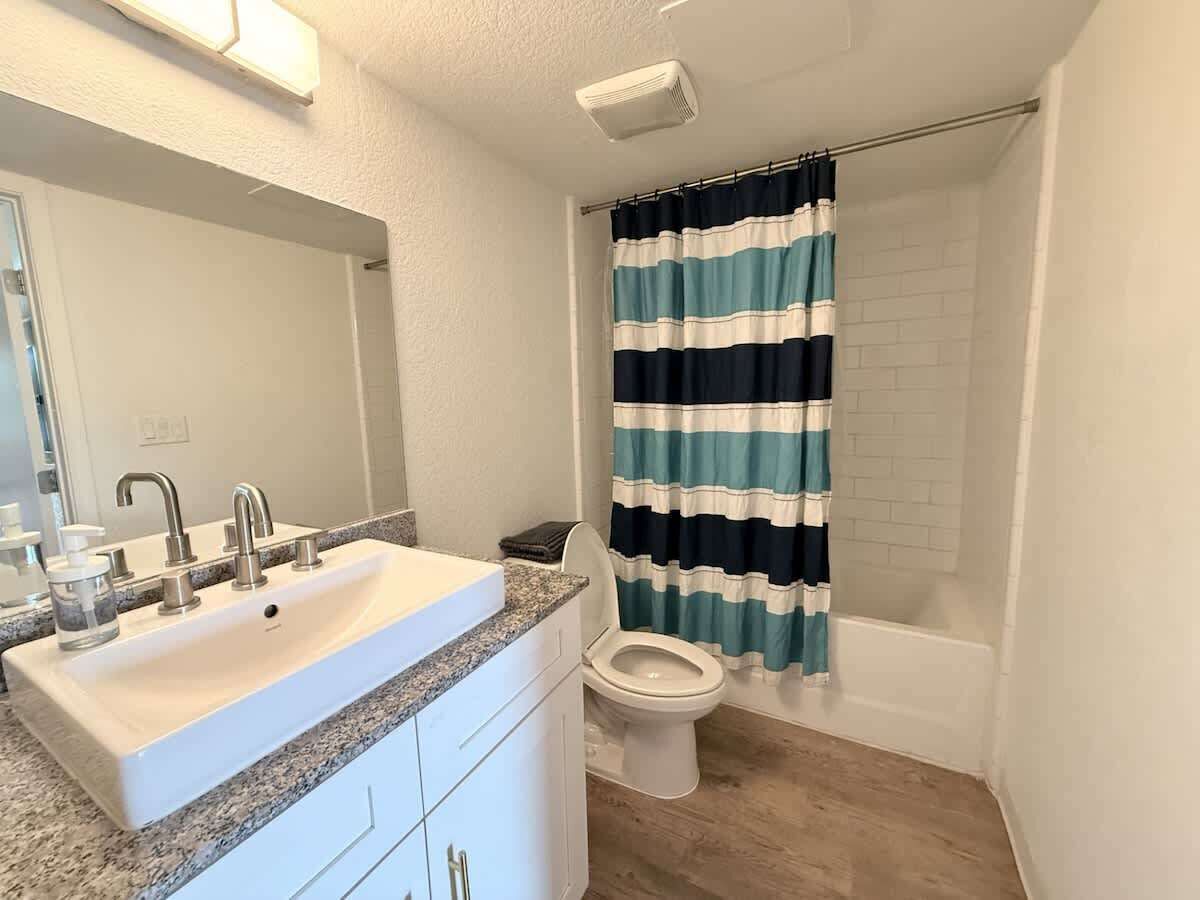 A bathroom with a white sink, two faucets, a mirror, a toilet, and a shower curtain.