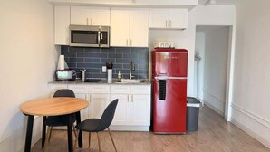 A compact kitchen with white cabinets, a red refrigerator, a microwave, and a small dining area with a table and chairs. - [50] ATX Studio: 1 Queen, Access to Gym & Laundry (Austin)