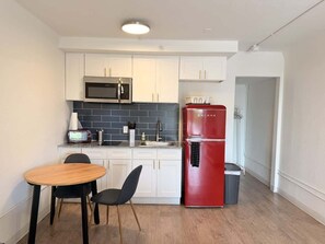 Eine kompakte Küche mit weißen Schränken, einem roten Kühlschrank, einer Mikrowelle und einem kleinen Essbereich mit Tisch und Stühlen.
