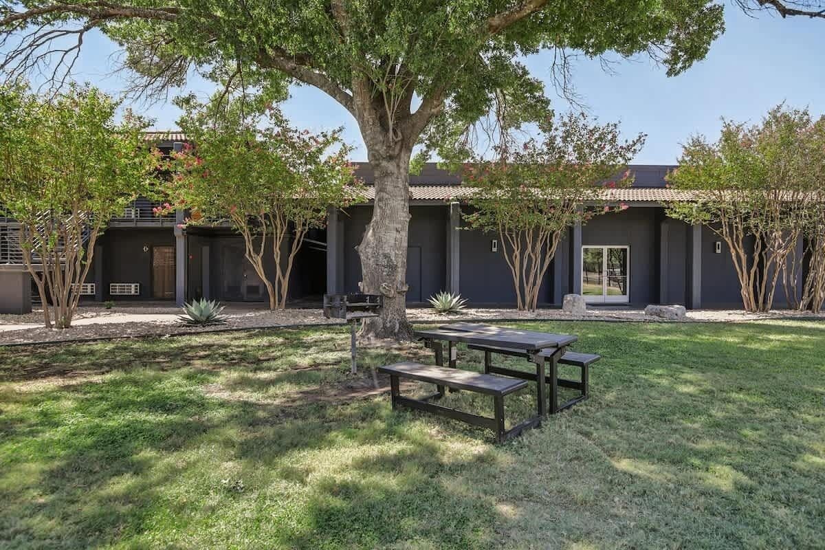 A modern building with a courtyard, outdoor seating, and a large tree.