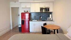 A compact kitchen with white cabinets, a red refrigerator, a microwave, and a small dining table with chairs. - [36] ATX Studio: 1 Queen, Access to Gym & Laundry (Austin)