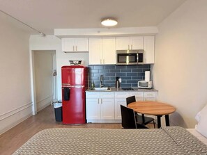 A compact kitchen with white cabinets, a red refrigerator, a microwave, and a small dining table with chairs. - [36] ATX Studio: 1 Queen, Access to Gym & Laundry (Austin)