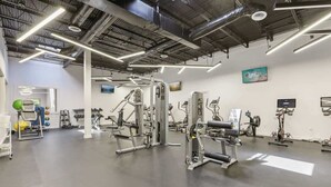 Un gimnasio con diversas máquinas de ejercicio, un televisor montado en la pared y un techo con vigas a la vista.