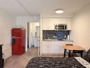 A compact kitchen with white cabinets, a red refrigerator, and a microwave. - [01] ATX Studio: 1 King, Dog Park, Laundry Access (Austin)