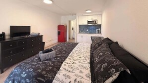 Een slaapkamer met een bed, een dressoir, een televisie en een kitchenette op de achtergrond.