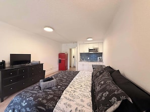 A bedroom with a bed, dresser, television, and a kitchenette in the background. - [23] ATX Studio: King Bed, Access to Gym & Laundry (Austin)