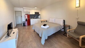 A compact hotel room with a bed, a small desk with a computer, a kitchenette, and a seating area. - [52] ATX Studio: 1 Queen, Access to Gym & Laundry (Austin)