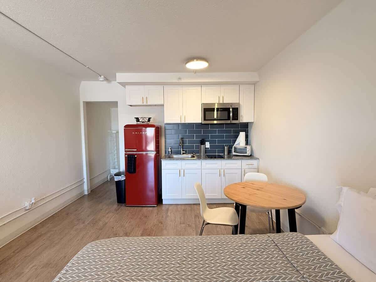 A compact kitchen with white cabinets, a red refrigerator, a microwave, and a small dining area with a round table and two chairs.