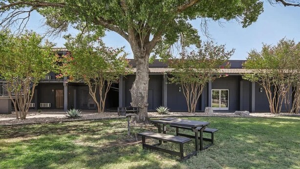 A modern building with a courtyard, outdoor seating, and a large tree. - [08] ATX Studio: 1 Queen, Dog Park, Laundry Access (Austin)