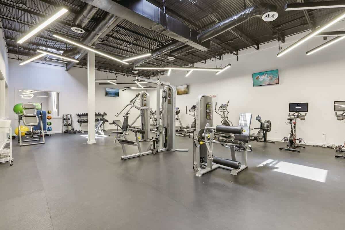 A gym with various exercise machines, a wall-mounted TV, and a ceiling with exposed beams.