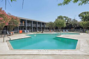 Ein Schwimmbecken mit einer Tiefe von 90 Zentimetern, umgeben von Liegestühlen und einem Gebäude mit Balkonen.