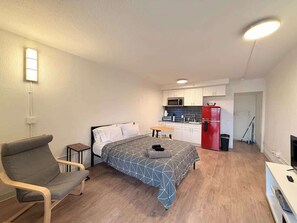 A compact room with a bed, a chair, a small table, a kitchenette with a microwave and a red refrigerator, and a TV. - [54] ATX Studio: 1 Queen, Access to Gym & Laundry (Austin)