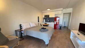 Une pièce de taille modeste comprenant un lit, une télévision, une petite table et, au fond, un coin cuisine.