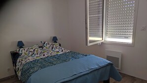 Et soveværelse med en seng, to sengeborde med lamper, et vindue med rullegardiner og en radiator.
