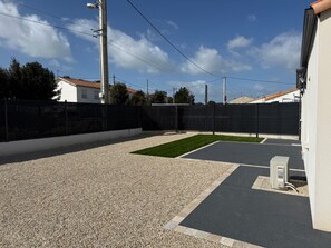 A parking area with a gravel surface, a paved section, and a black fence.