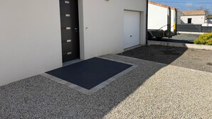 En bygning med en sort dør, en hvid garagedør og en grusbelagt indkørsel.